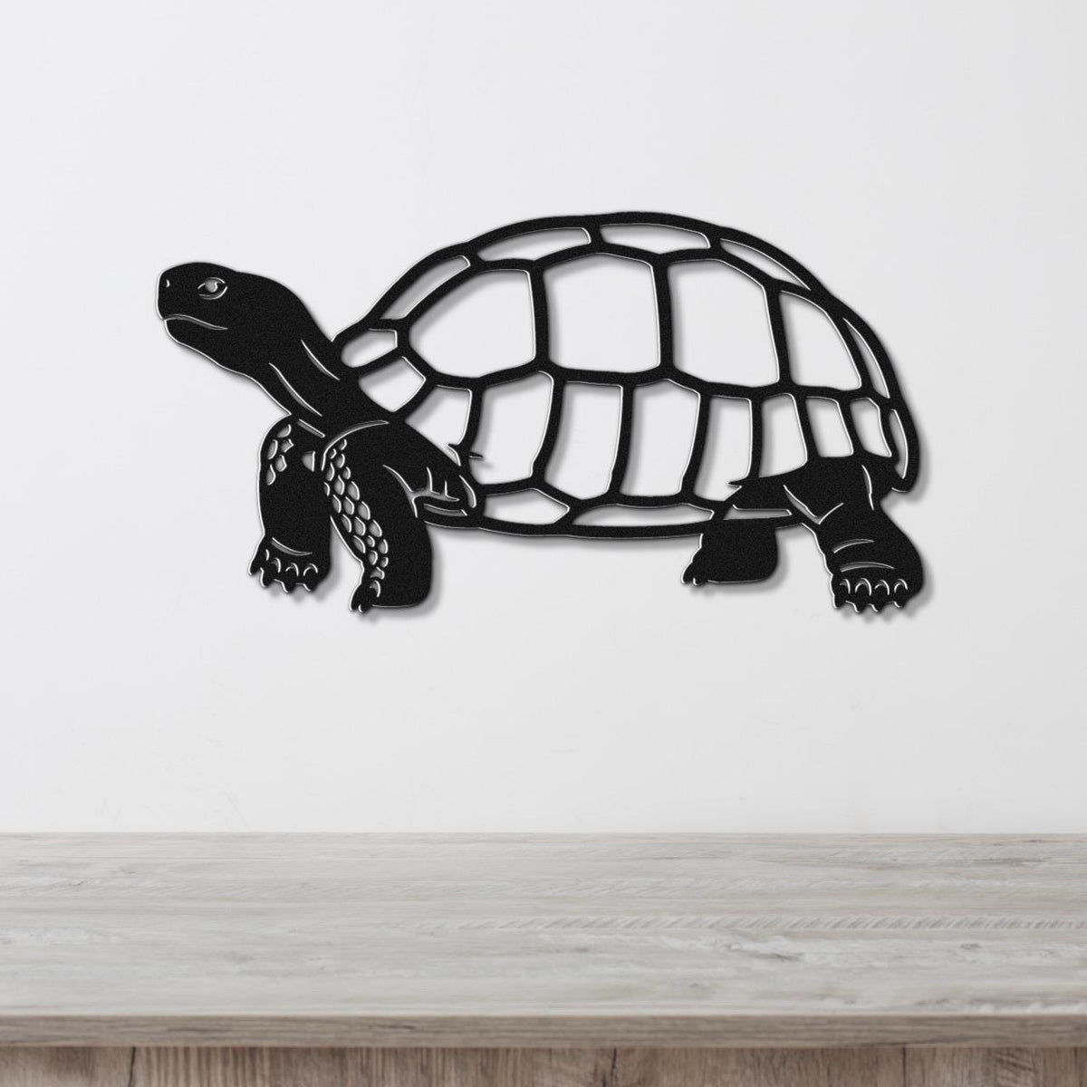 Black metal tortoise wall art with a cutout shell and detailed legs, mounted on a white wall above a wooden surface.