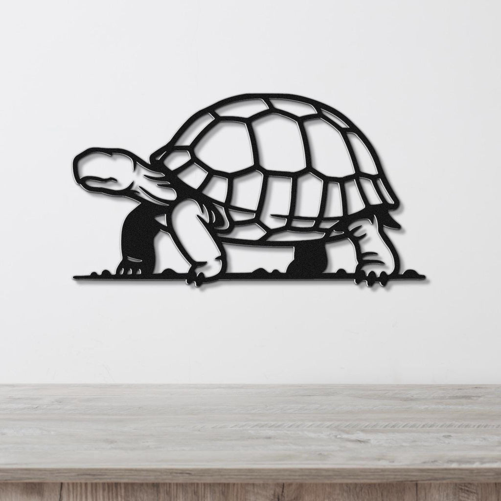 Black metal tortoise wall art with a cutout shell and legs, mounted on a white wall above a light wood surface.