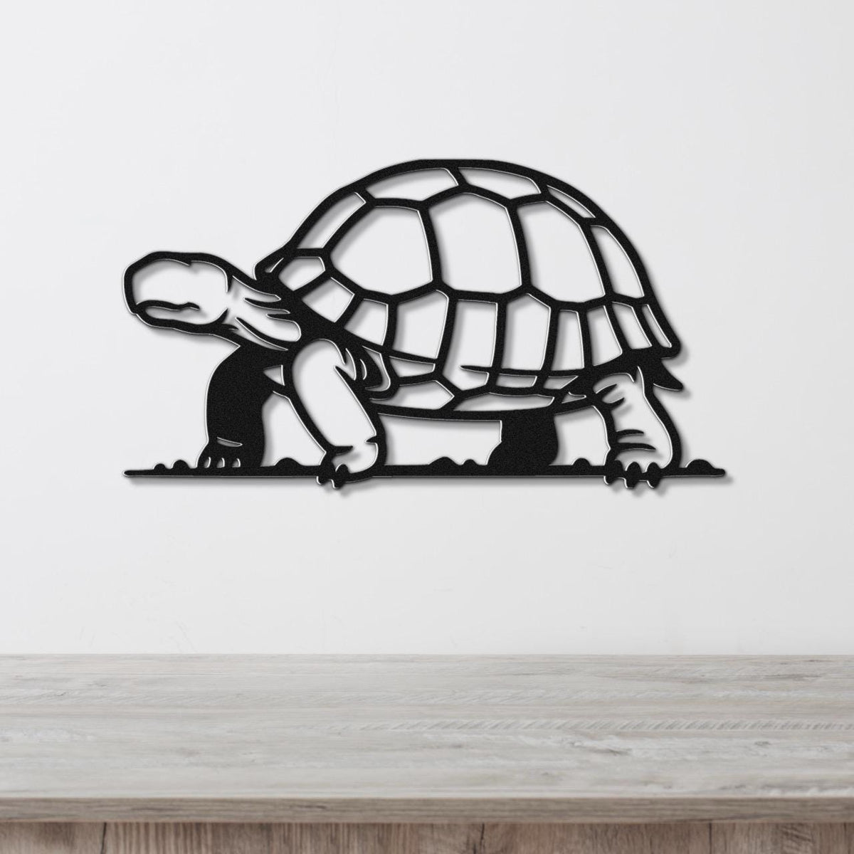 Black metal tortoise wall art with a cutout shell and legs, mounted on a white wall above a light wood surface.