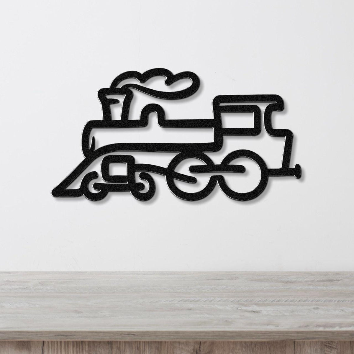 Black metal train wall art with a silhouette design of a steam locomotive, mounted on a white wall above a wooden surface.