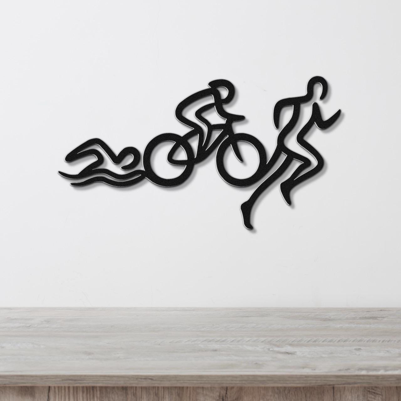 Black metal wall art featuring a triathlon silhouette of swim, bike, and run figures, mounted on a white wall above a wooden surface.
