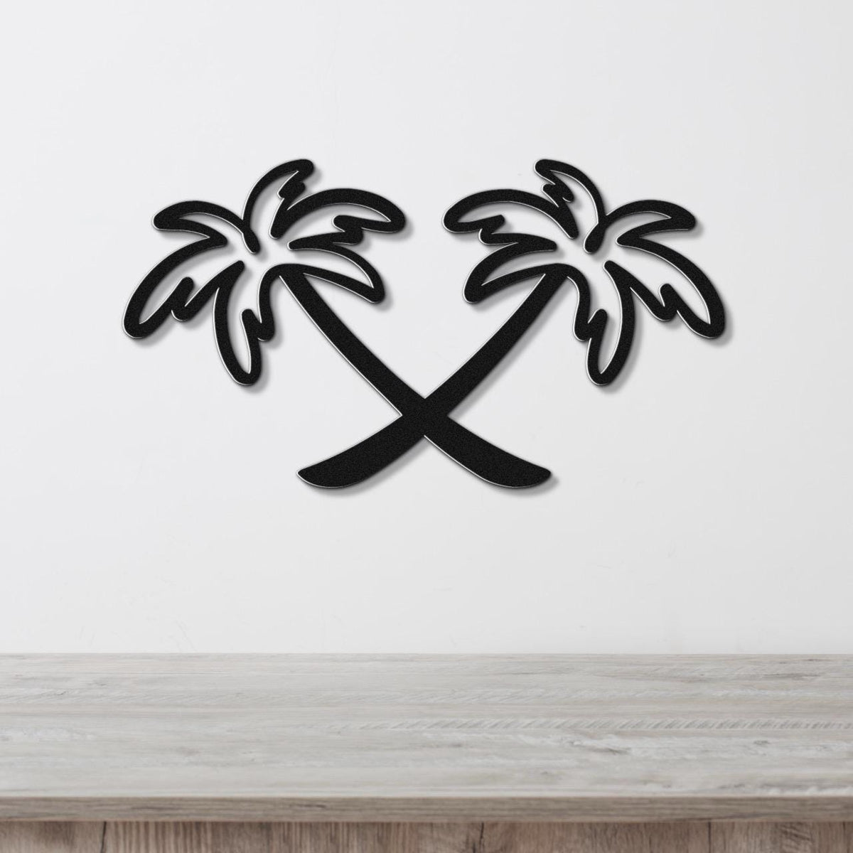 Black metal wall art featuring two crossed palm trees in a silhouette style, mounted on a white wall above a light wood surface.