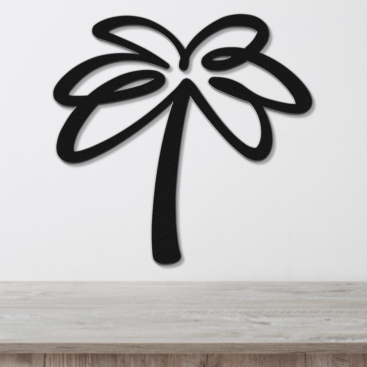 Black metal palm tree wall art with leaf cutouts, mounted on a white wall above a light wood surface.