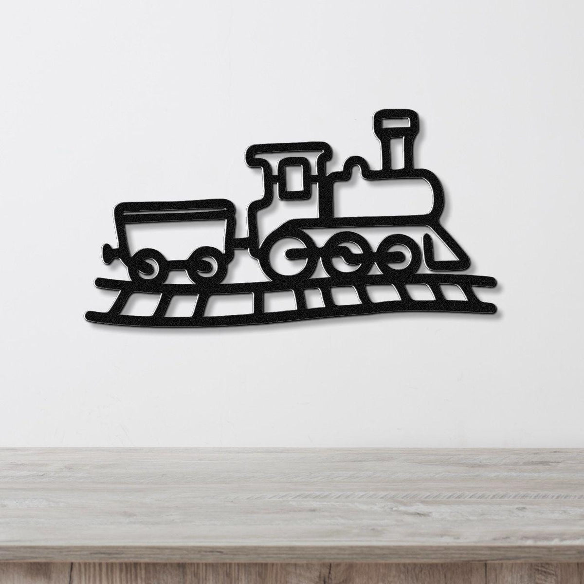 Black metal train wall art with a silhouette design of a locomotive and car on tracks, mounted on a white wall above a wooden surface.