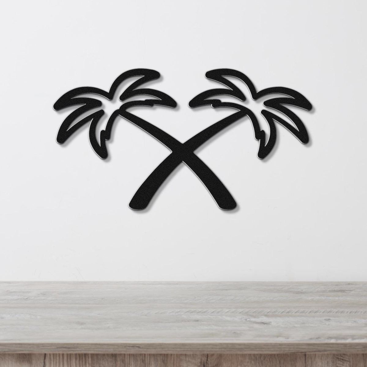 Black metal wall art featuring two crossed palm trees in a silhouette style, mounted on a white wall above a light wood surface.