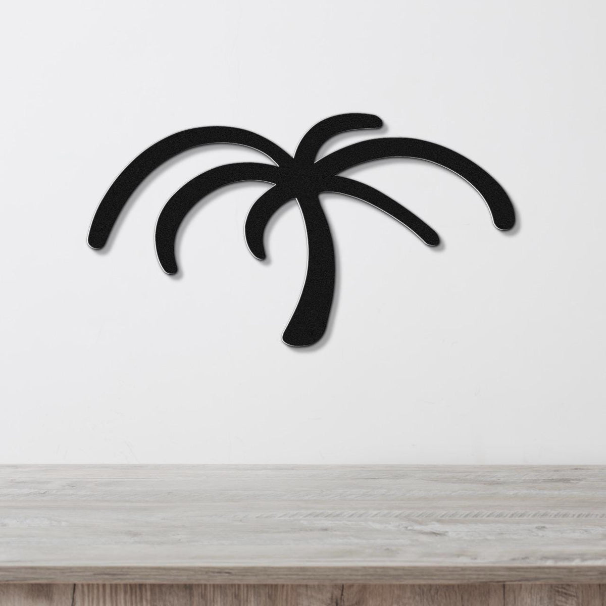 Black metal palm tree wall art with curved frond cutouts, mounted on a white wall above a light wood surface.