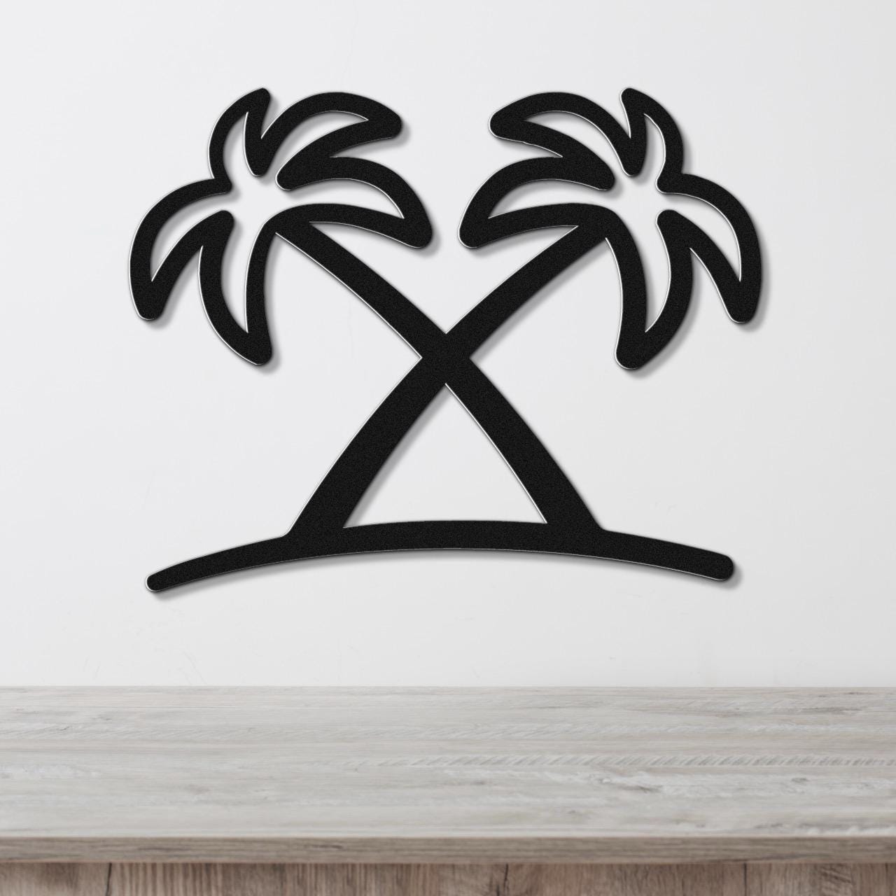 Black metal wall art featuring a silhouette of two crossed palm trees with leafy fronds, mounted on a white wall above a light wood surface.