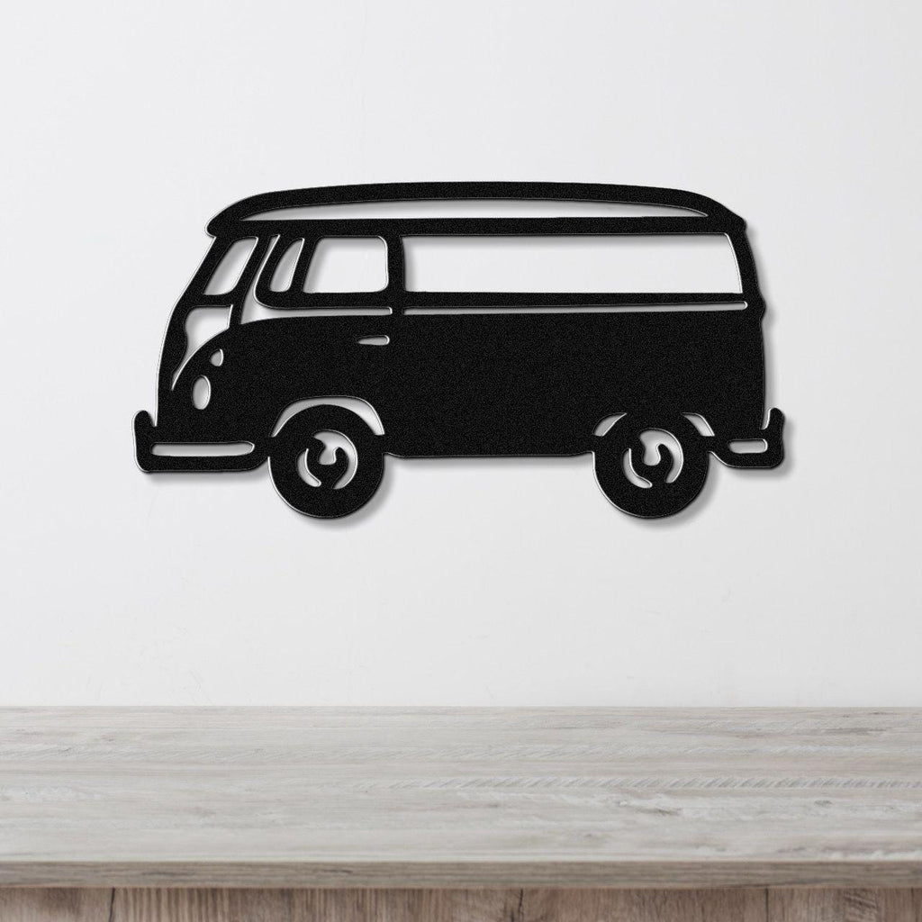 Black metal wall art cutout of a vintage van with visible windows and wheels, mounted on a white wall above a light wood surface.