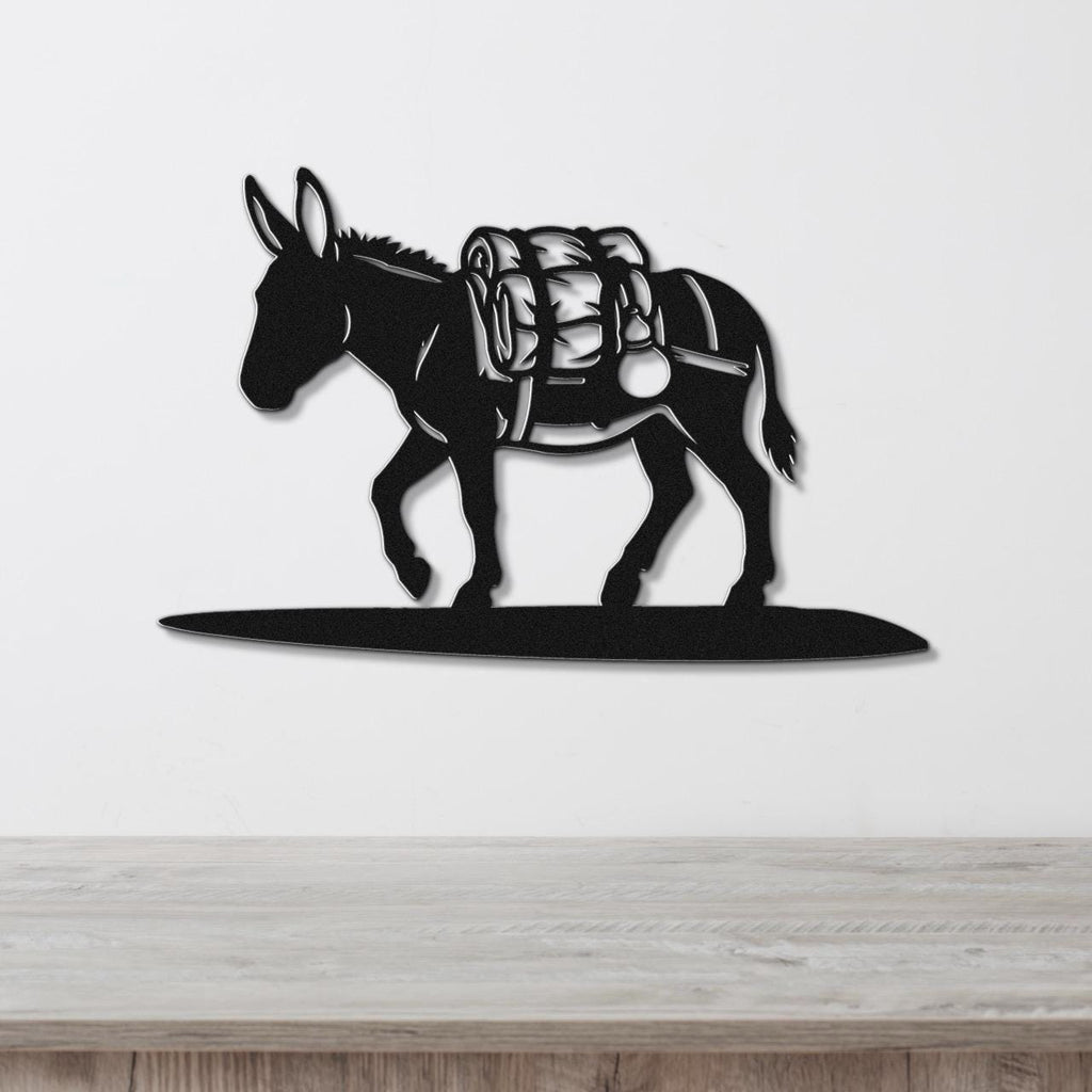 Black metal burro wall art silhouette with saddle and pack details, mounted on a white wall above a wooden surface.