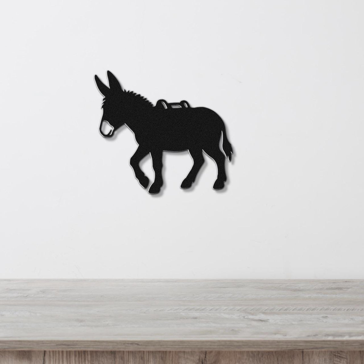 Black metal burro silhouette wall art with saddle cutout, mounted on a white wall above a light wood counter.