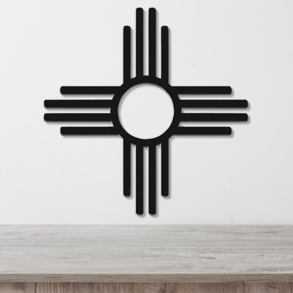 Black metal Zia Sun symbol wall art with a bold circular cutout and radiating rays, mounted on a white wall above a light wood surface.