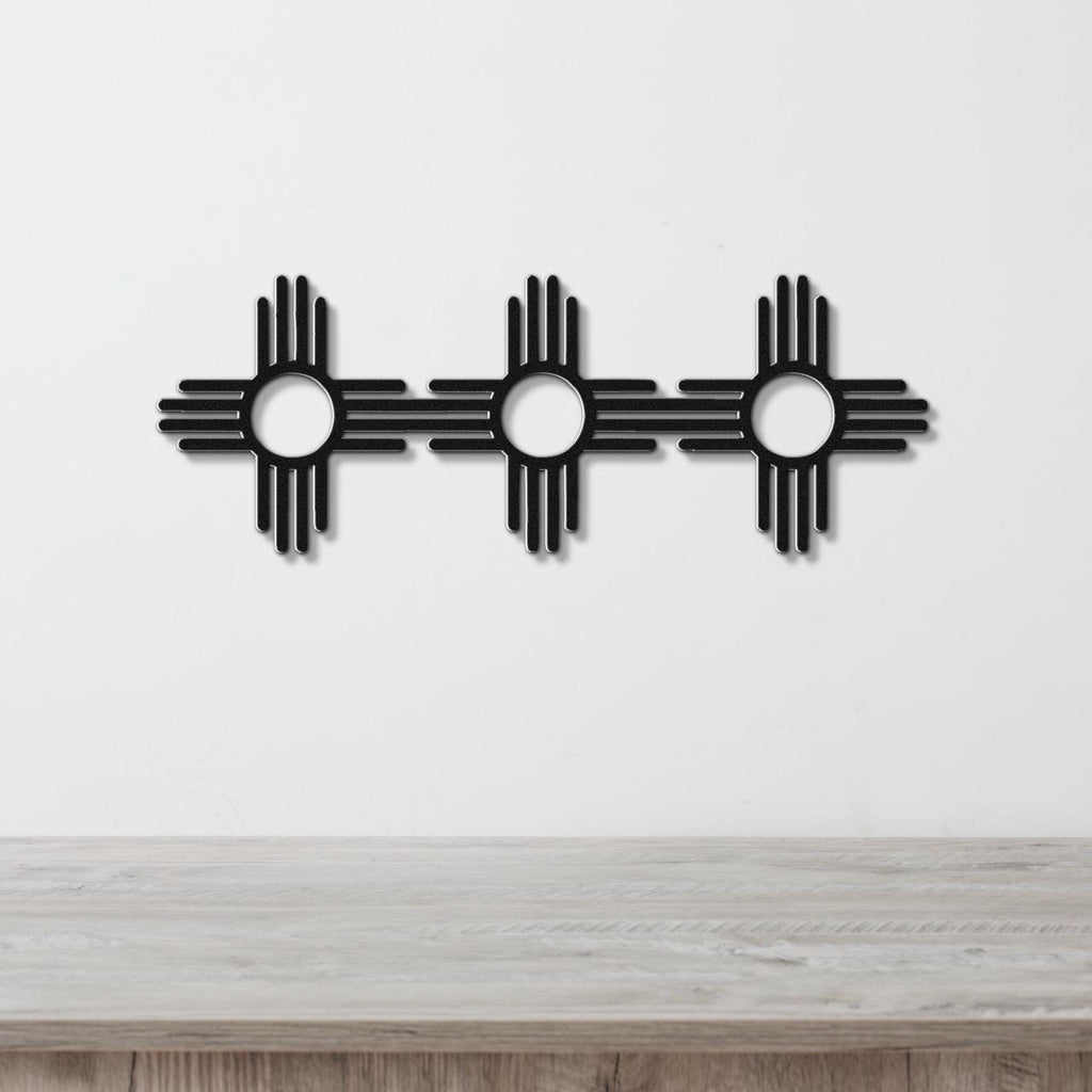 Black metal wall art featuring three Zia Sun symbols in a row, each with a central circle and four rays, mounted on a white wall above a wooden surface.