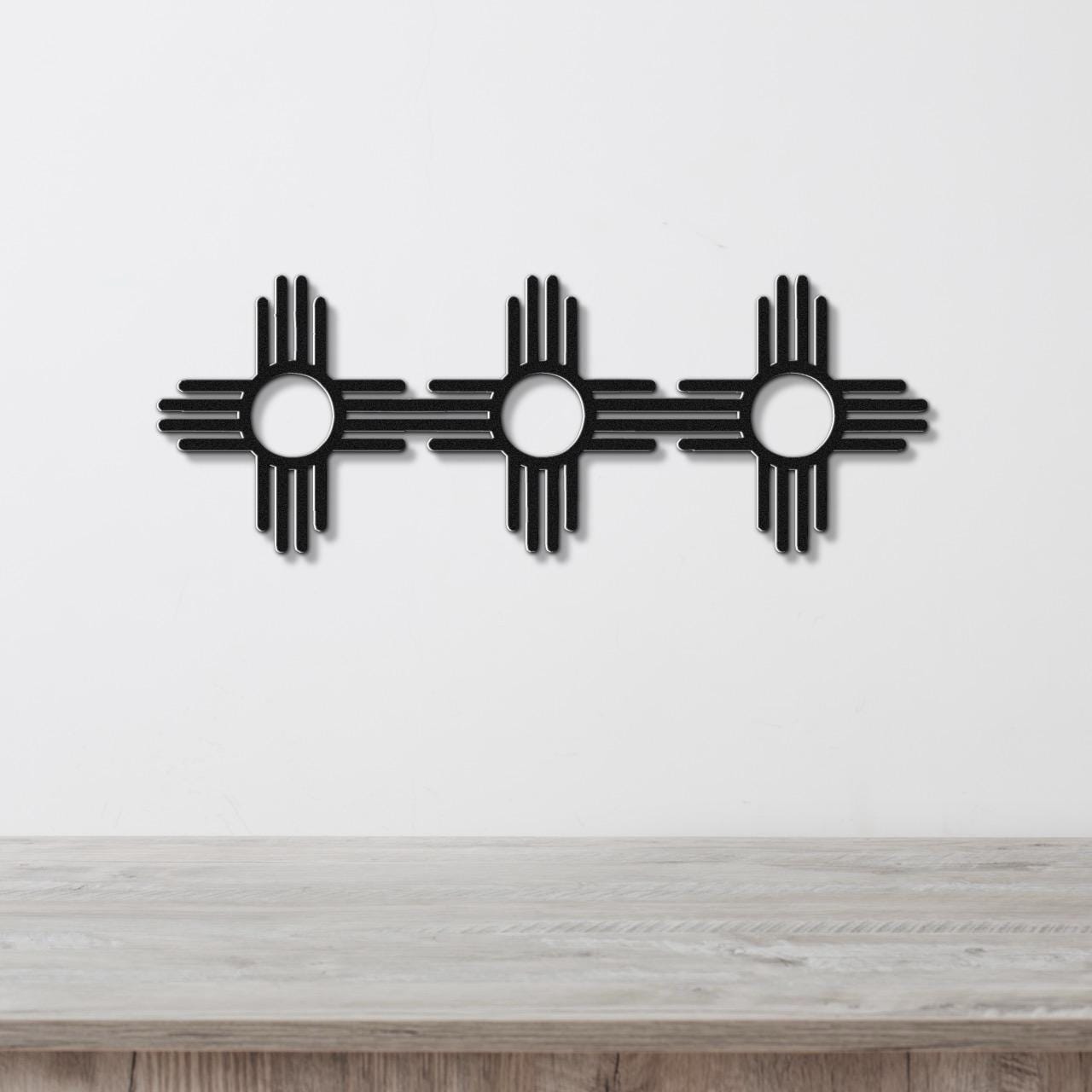 Black metal wall art featuring three Zia Sun symbols in a row, each with a central circle and four rays, mounted on a white wall above a wooden surface.