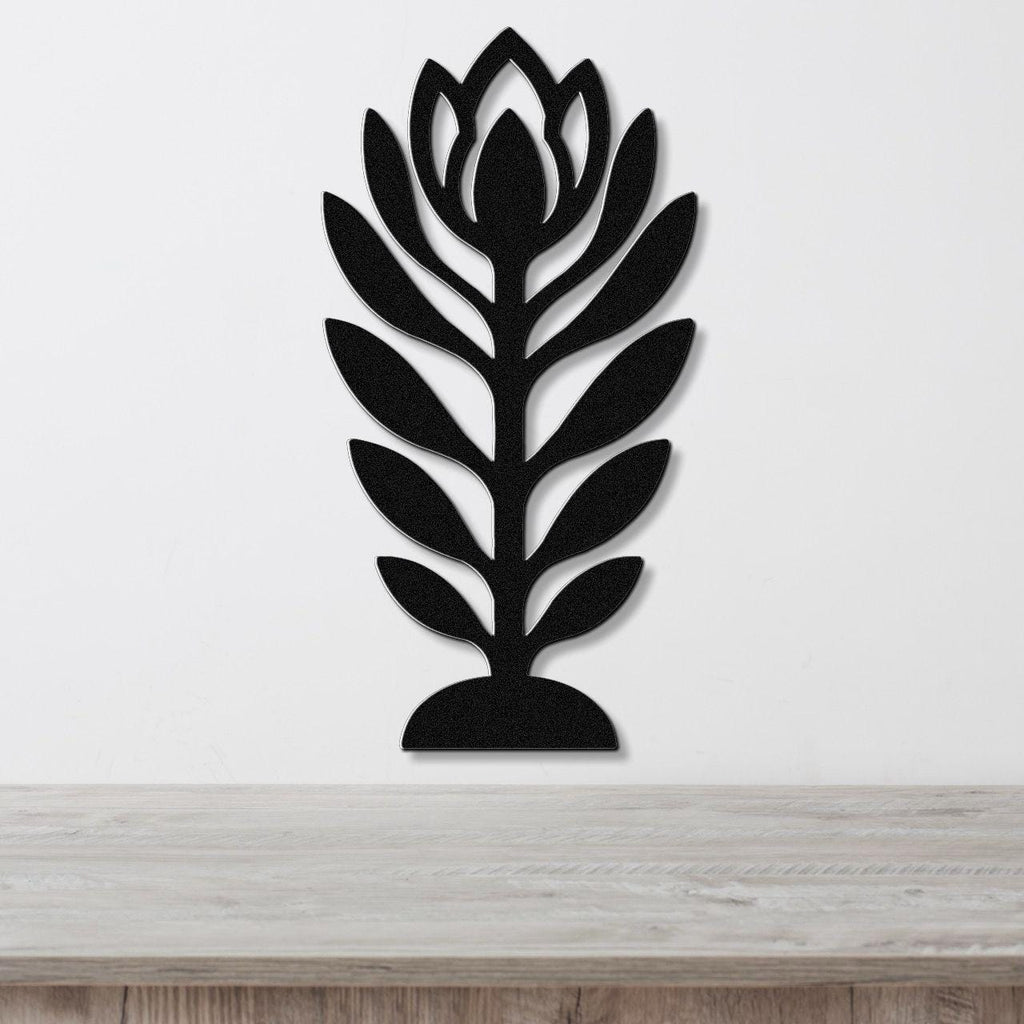 Black metal wall art in a stylized wildflower silhouette with layered leaf and bloom cutouts, mounted on a white wall above a light wood surface.