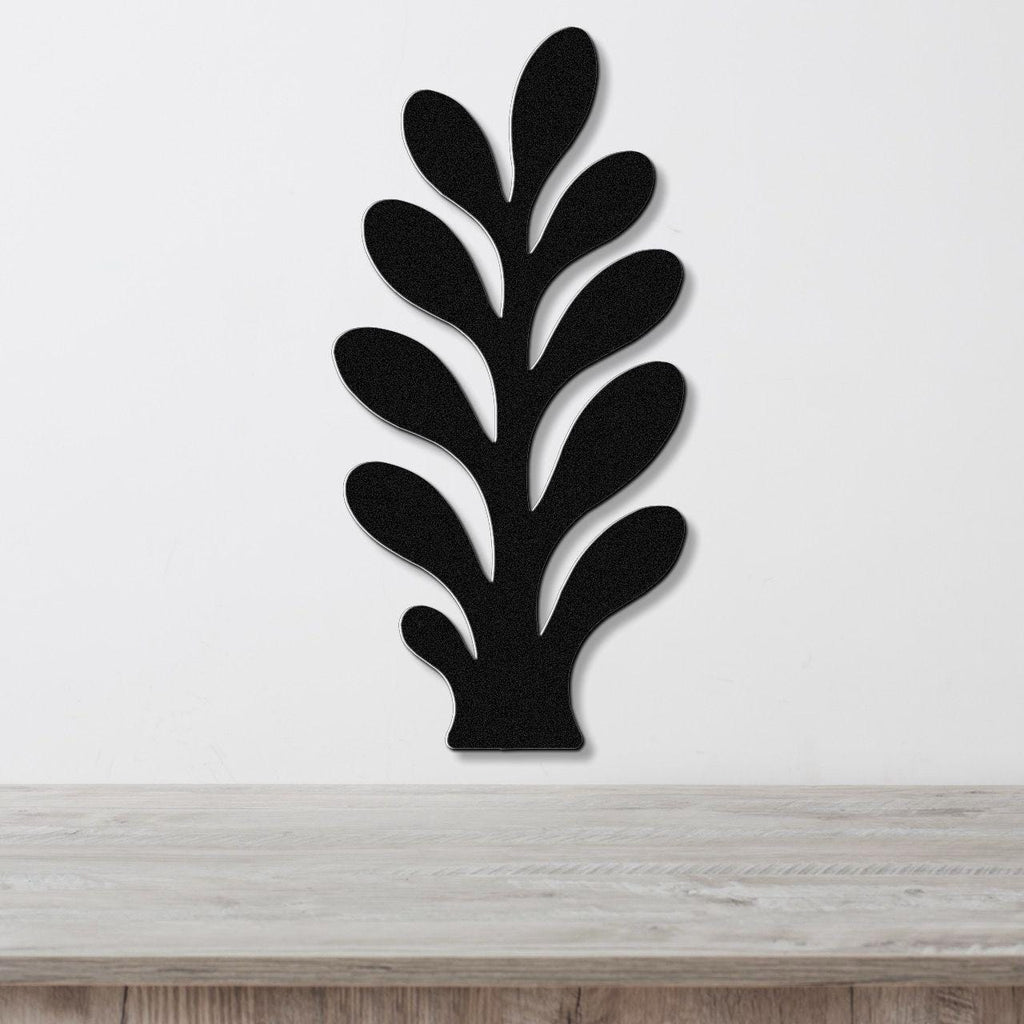 Black metal wall art in a leafy sprig silhouette with cutout details, mounted on a white wall above a light wood surface.