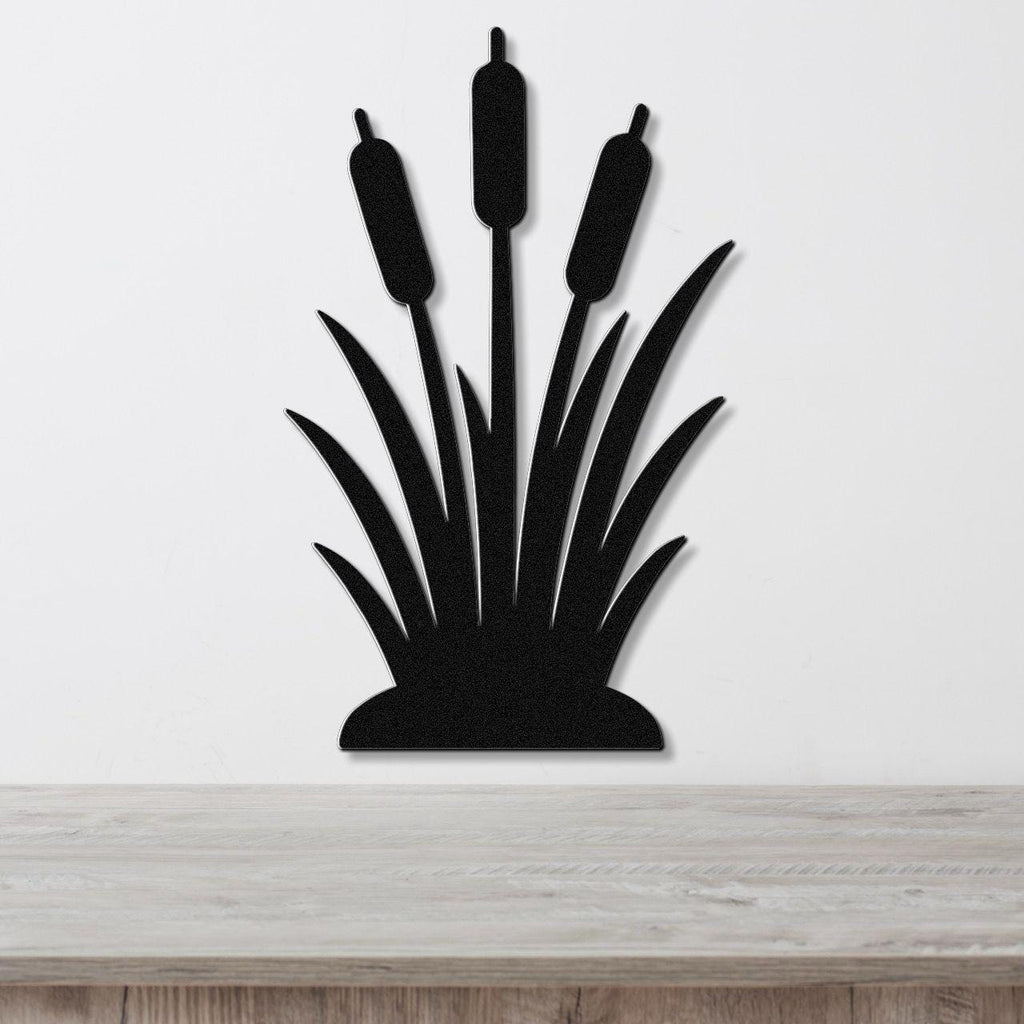 Black metal wall art silhouette of cattails with three seed heads and long leaves, mounted on a white wall above a light wood surface.