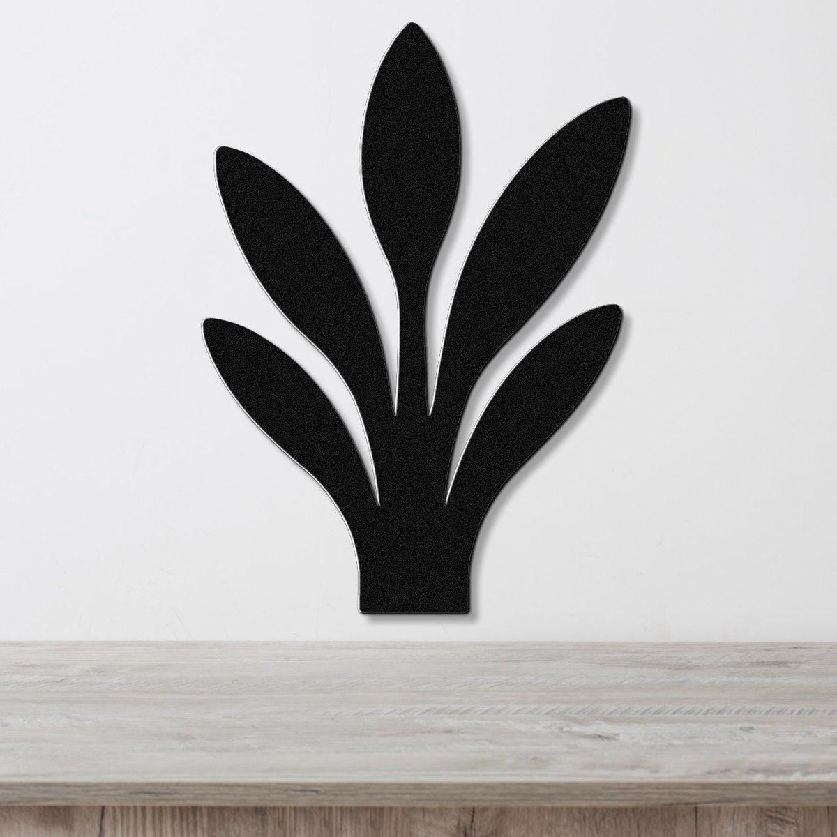 Black metal wall art in a snake plant silhouette with five leaf cutouts, mounted on a white wall above a light wood surface.