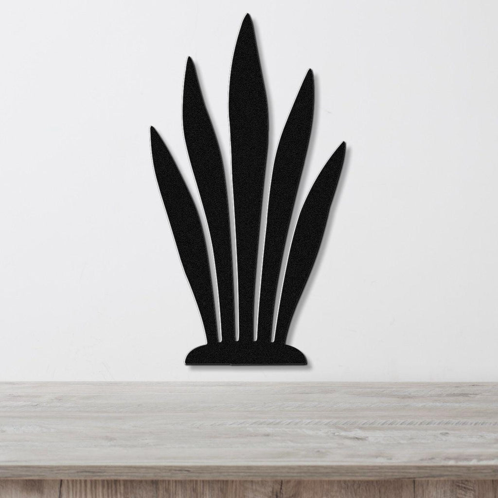 Black metal wall art in a snake plant silhouette with five tall, pointed leaves, mounted on a white wall above a light wood surface.