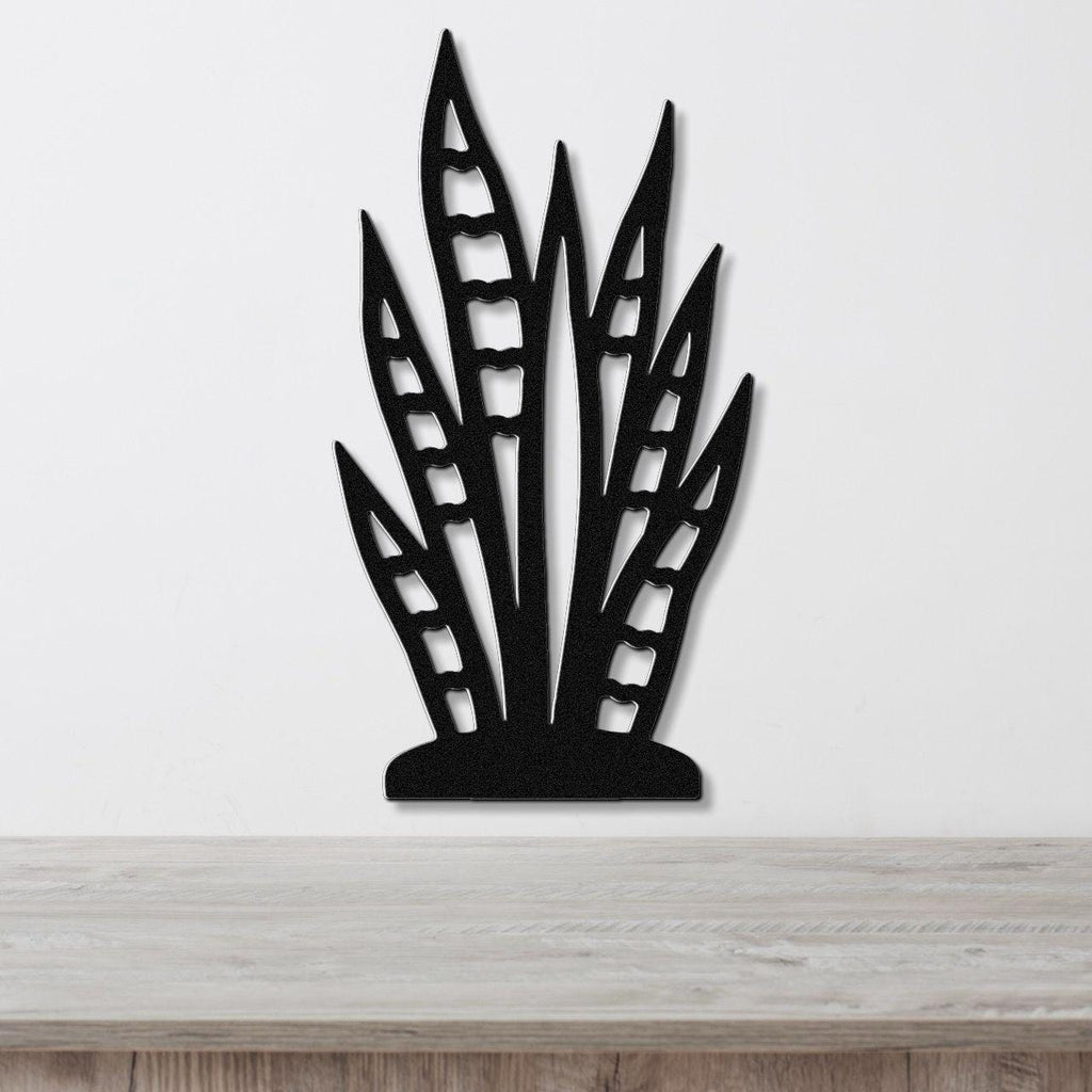 Black metal wall art cutout of a snake plant with leaf-shaped openings, mounted on a white wall above a wooden surface.