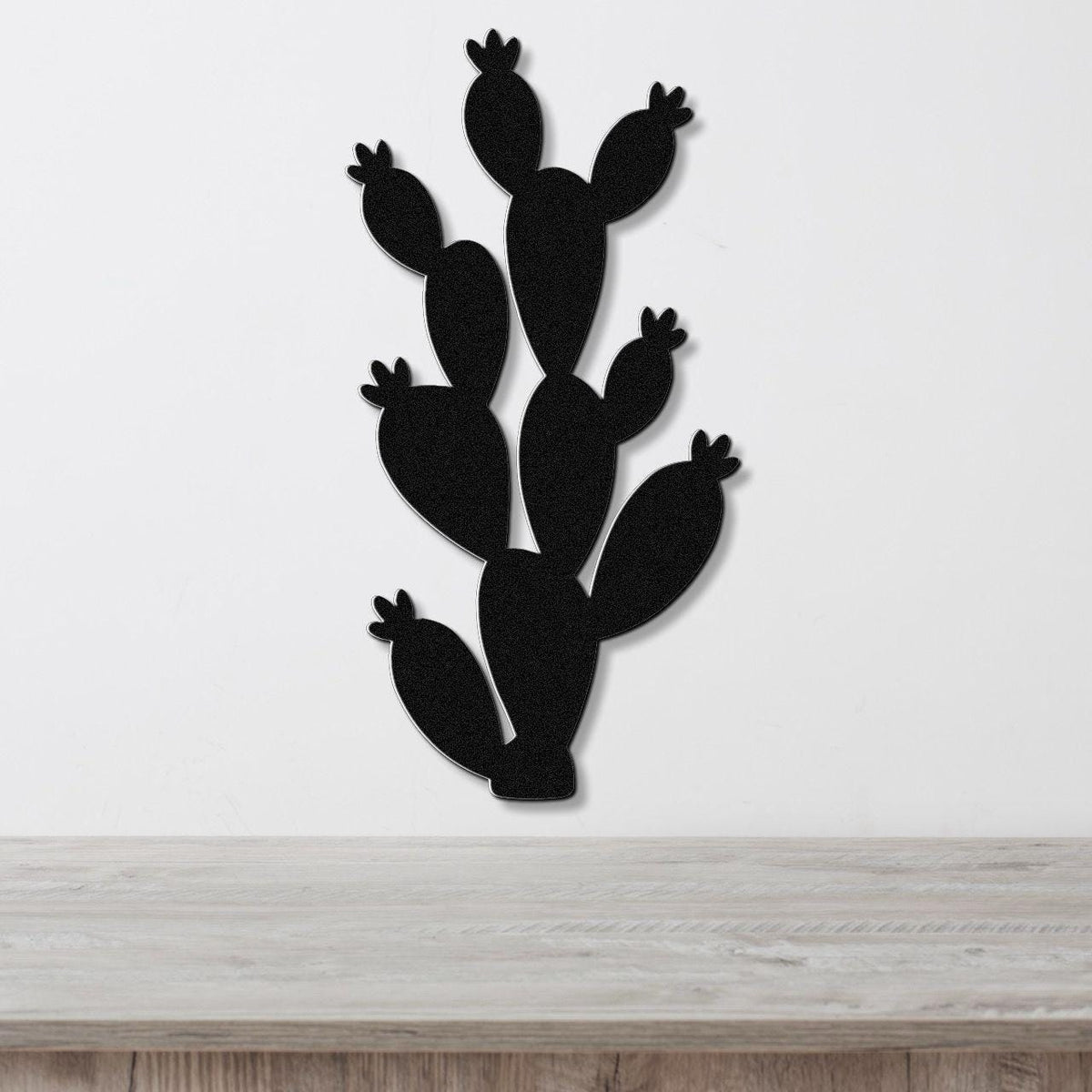 Black metal cactus wall art with multiple paddle-shaped segments and small flower cutouts, mounted on a white wall above a light wood surface.