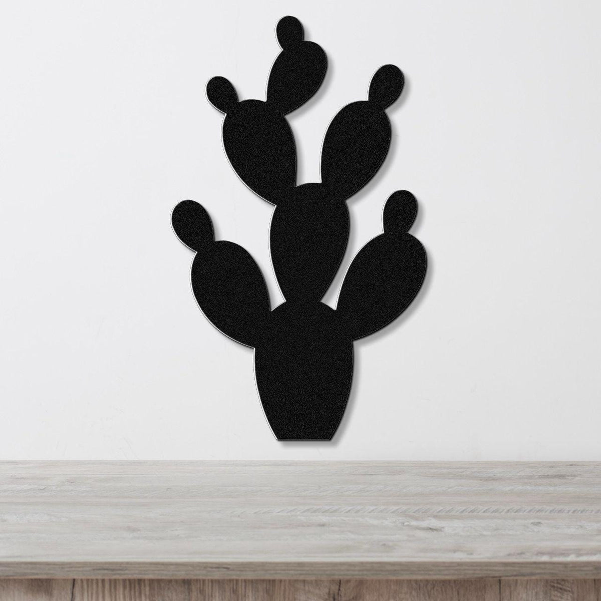 Black metal prickly pear cactus wall art with cutout pads, mounted on a white wall above a light wood counter.