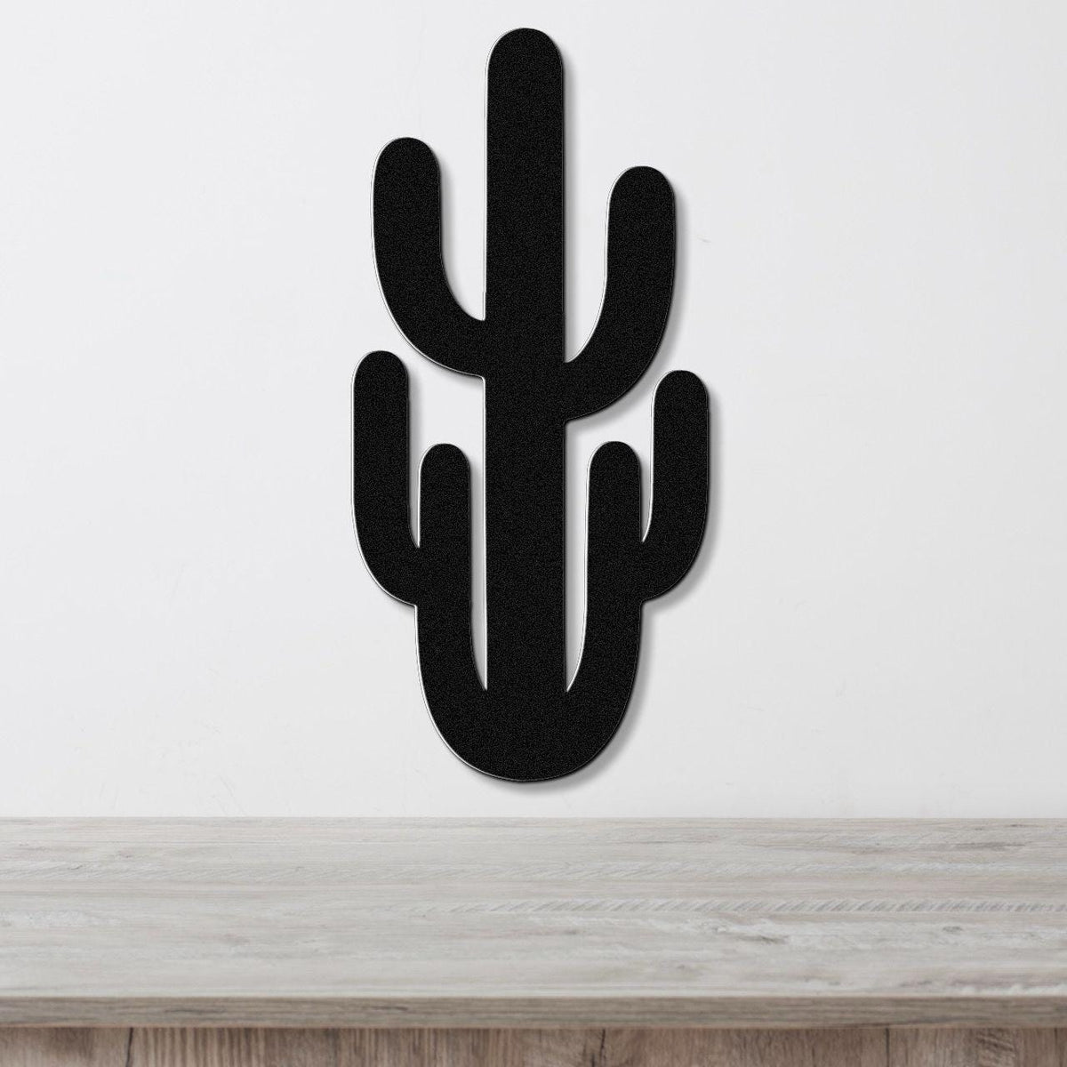 Black metal Saguaro cactus wall art with cutout arms, mounted on a white wall above a light wood counter.