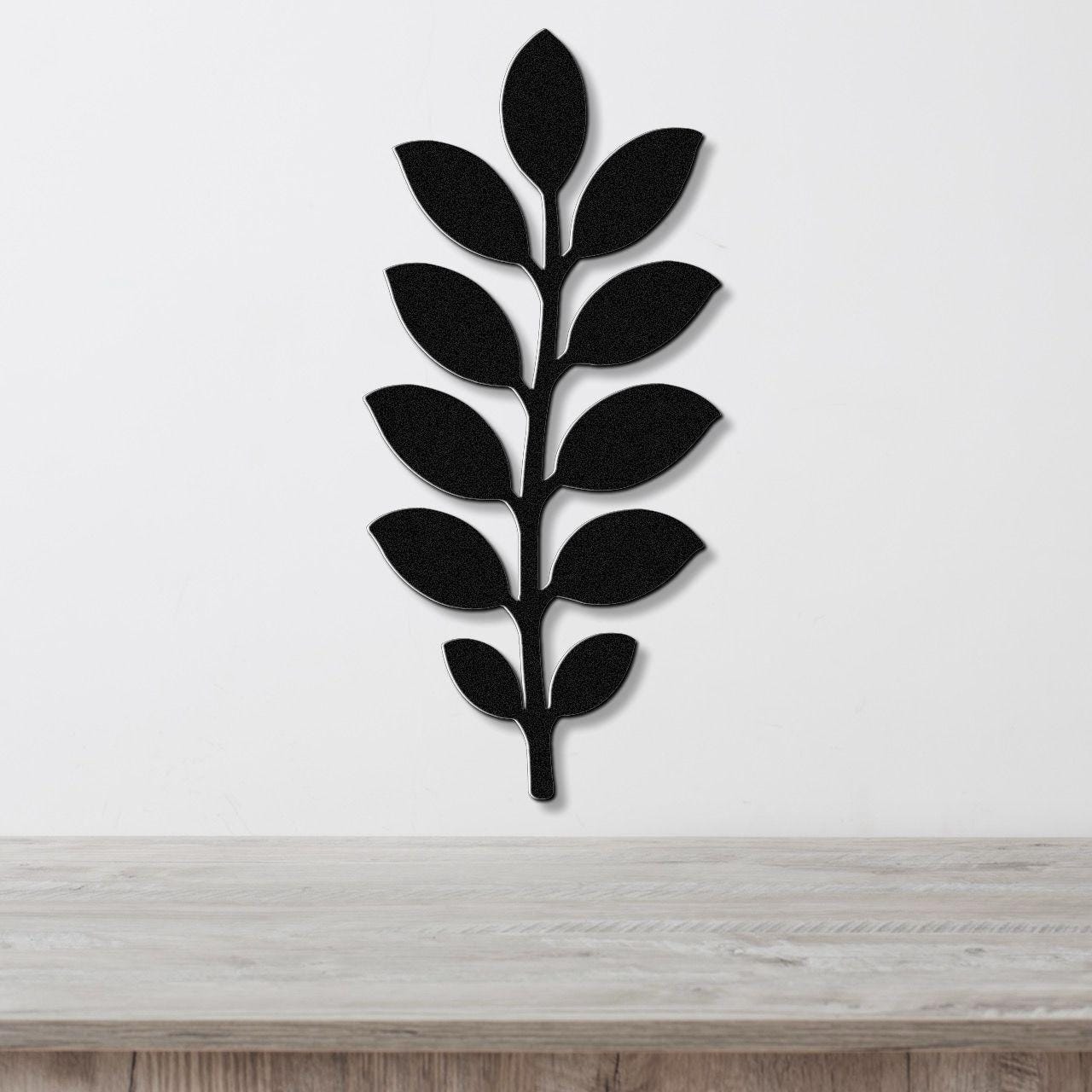 Black metal wall art in the shape of a leafy branch, mounted on a white wall above a light wood surface.