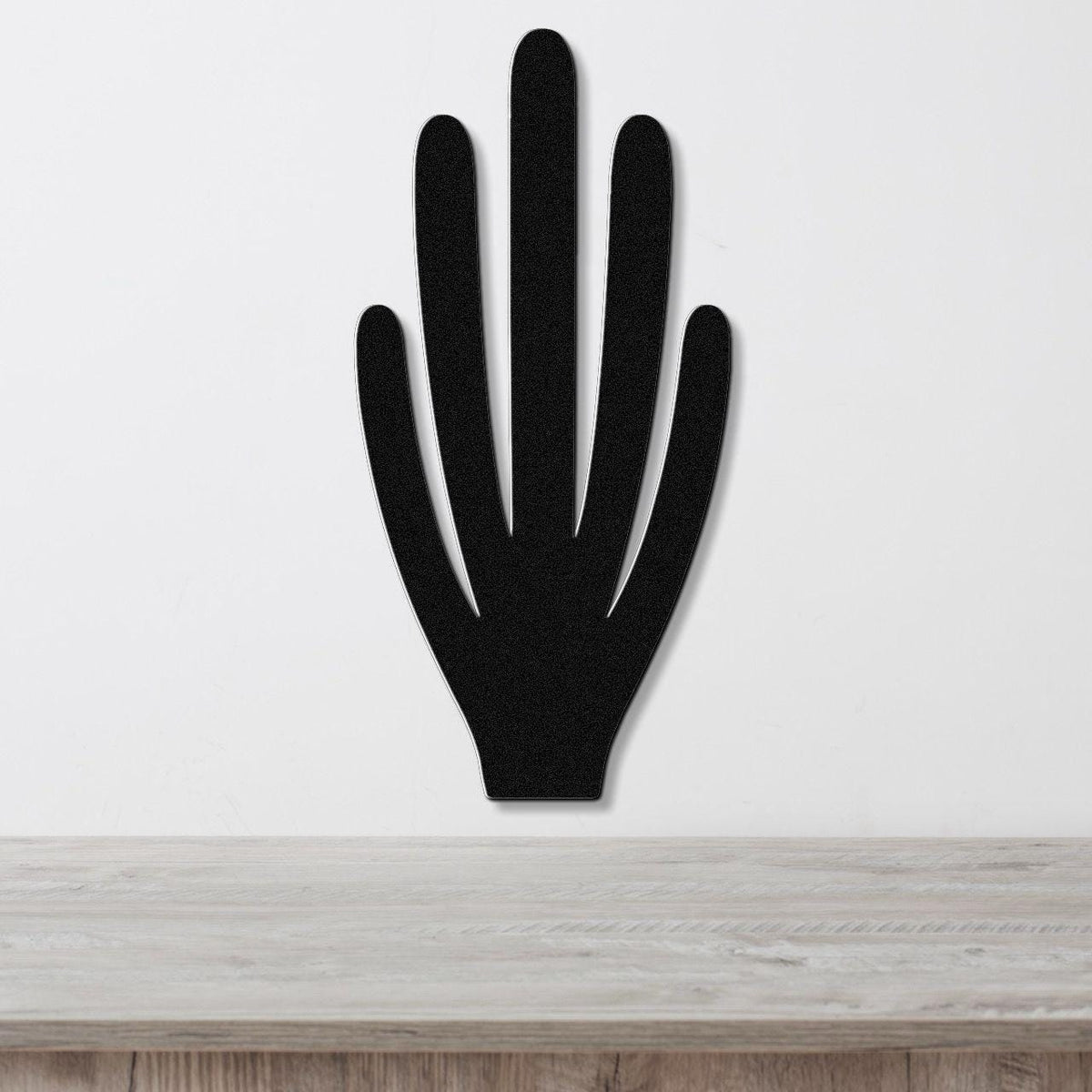Black metal wall art in the shape of a hand with five fingers, mounted on a white wall above a wooden surface.