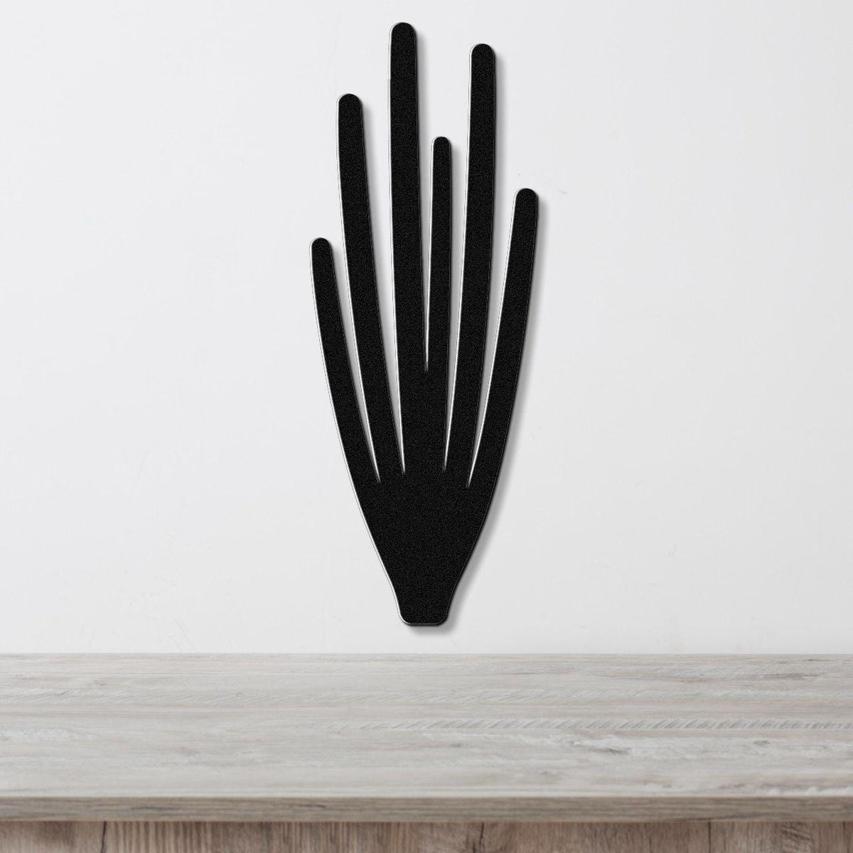 Black metal wall art cutout of an organ pipe cactus with vertical spines, mounted on a white wall above a light wood surface.