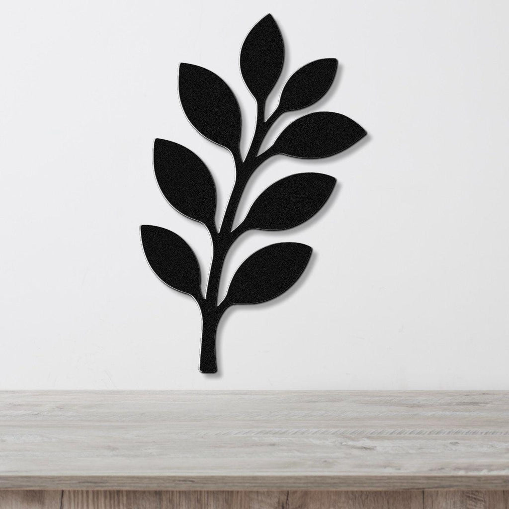 Black metal wall art in the shape of an olive branch with leaf cutouts, mounted on a white wall above a light wood surface.