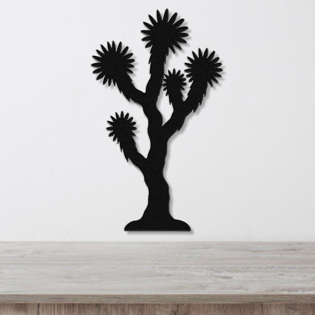 Black metal Joshua tree wall art with spiky branch cutouts, mounted on a white wall above a light wood countertop.
