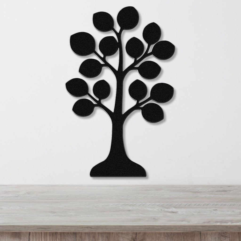 Black metal wall art in the shape of a tree with leaf cutouts, mounted on a white wall above a light wood surface.