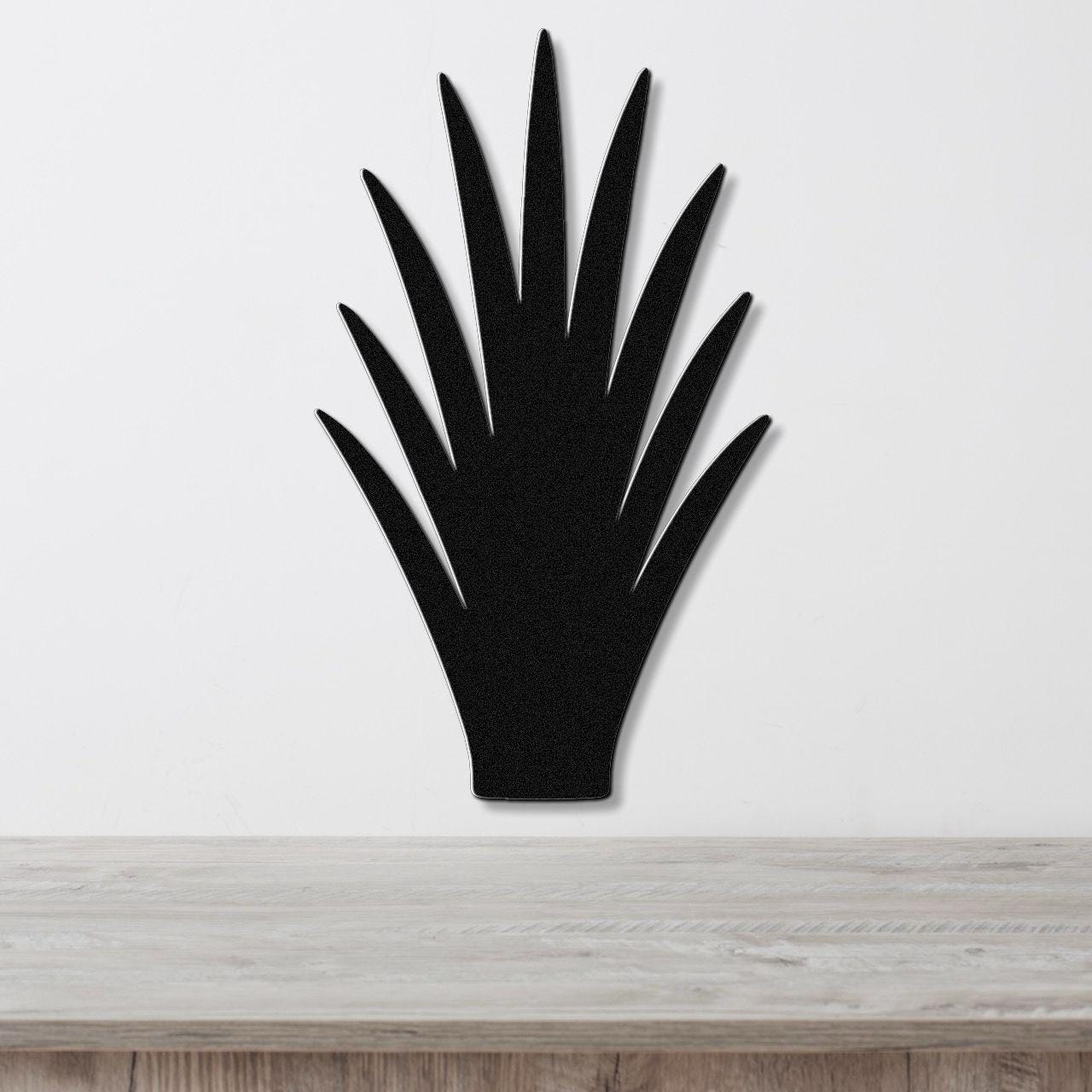 Black metal wall art in the silhouette of a spiky desert plant, mounted on a white wall above a light wood surface.