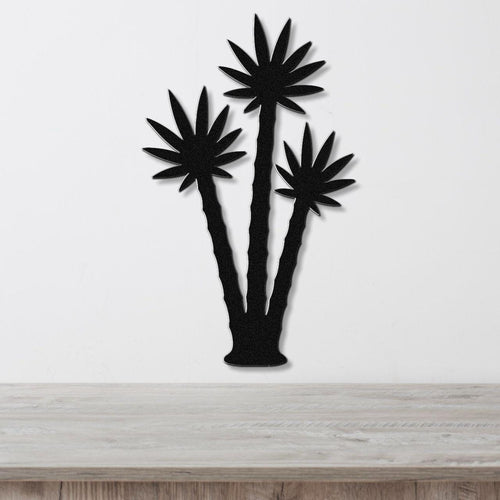Black metal wall art featuring a silhouette of three palm trees with leaf cutouts, mounted on a white wall above a wooden surface.