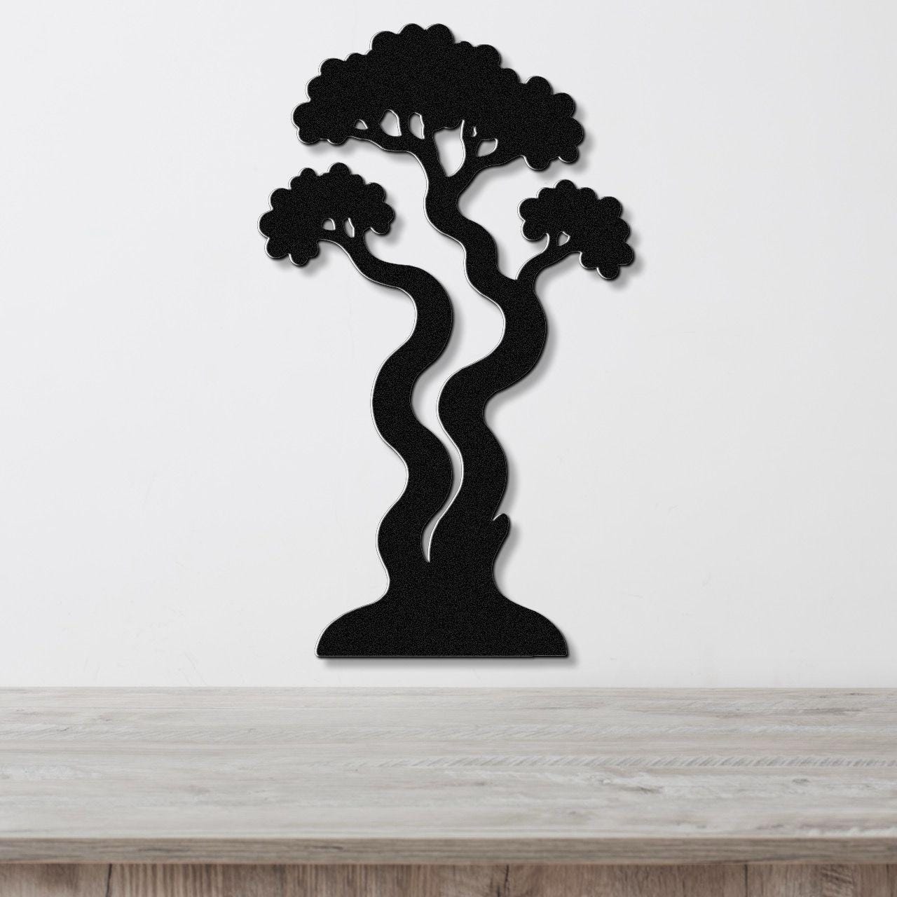 Black metal wall art in a bonsai tree silhouette with wavy trunk and layered branches, mounted on a white wall above a light wood surface.