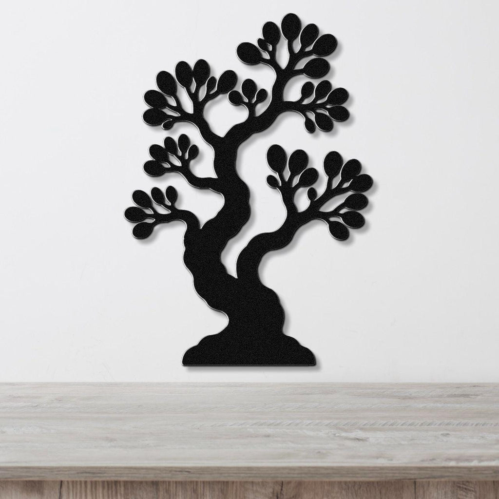 Black metal wall art in the shape of a bonsai tree with detailed branch and leaf cutouts, mounted on a white wall above a wooden surface.