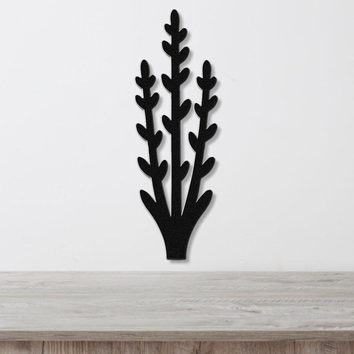 Black metal wall art in a silhouette of an abstract desert plant with branching stems and leaf cutouts, mounted on a white wall above a light wood surface.