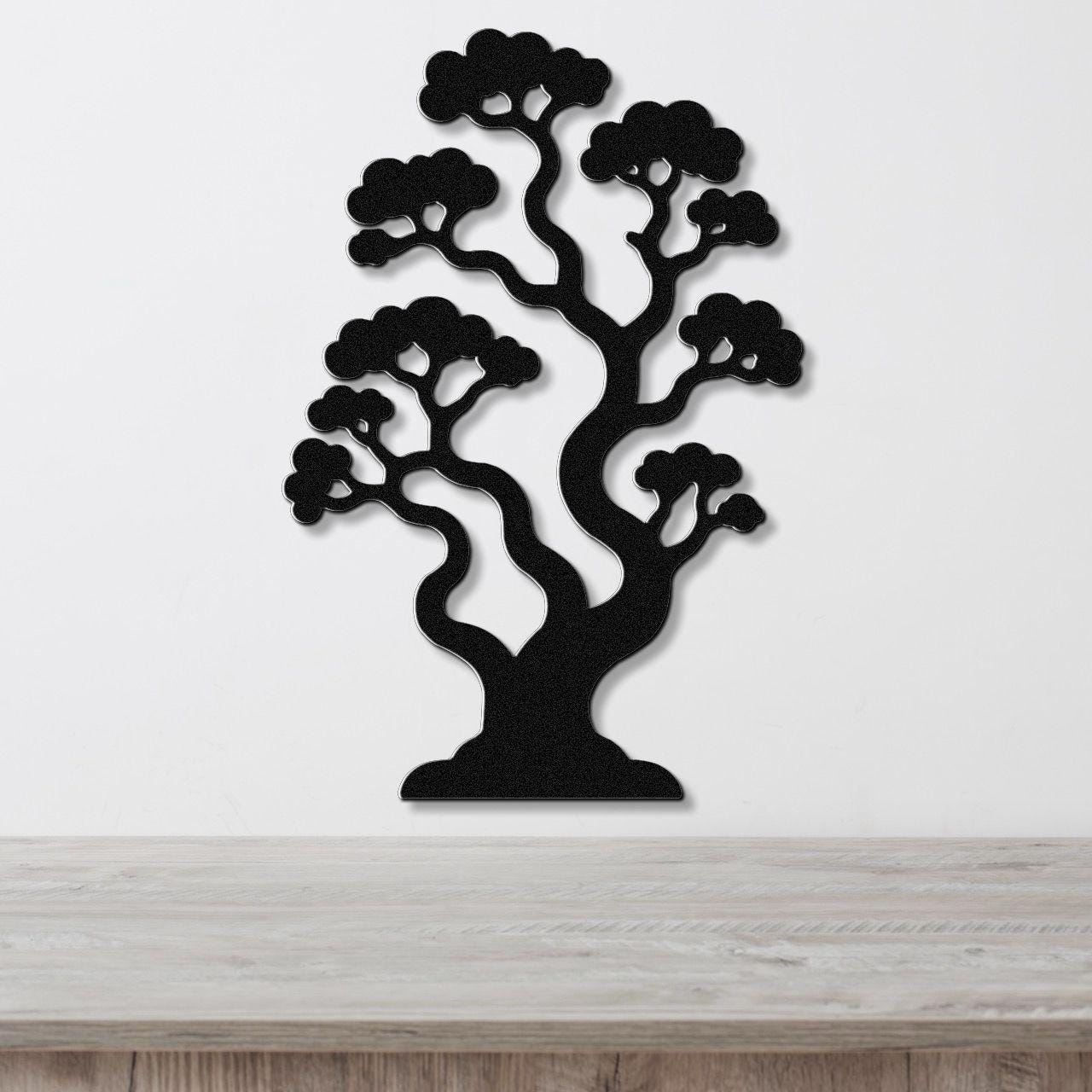 Black metal wall art sculpture of a bonsai tree with layered branches and cloud-like foliage, mounted on a white wall above a light wood surface.