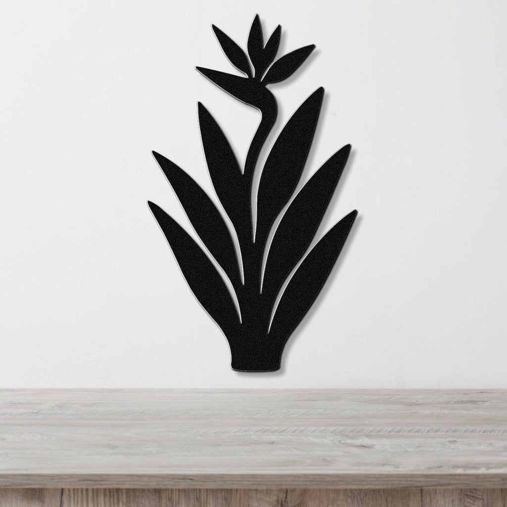 Black metal Bird of Paradise wall art with a silhouette cutout of leaves and flower, mounted on a white wall above a light wood counter.