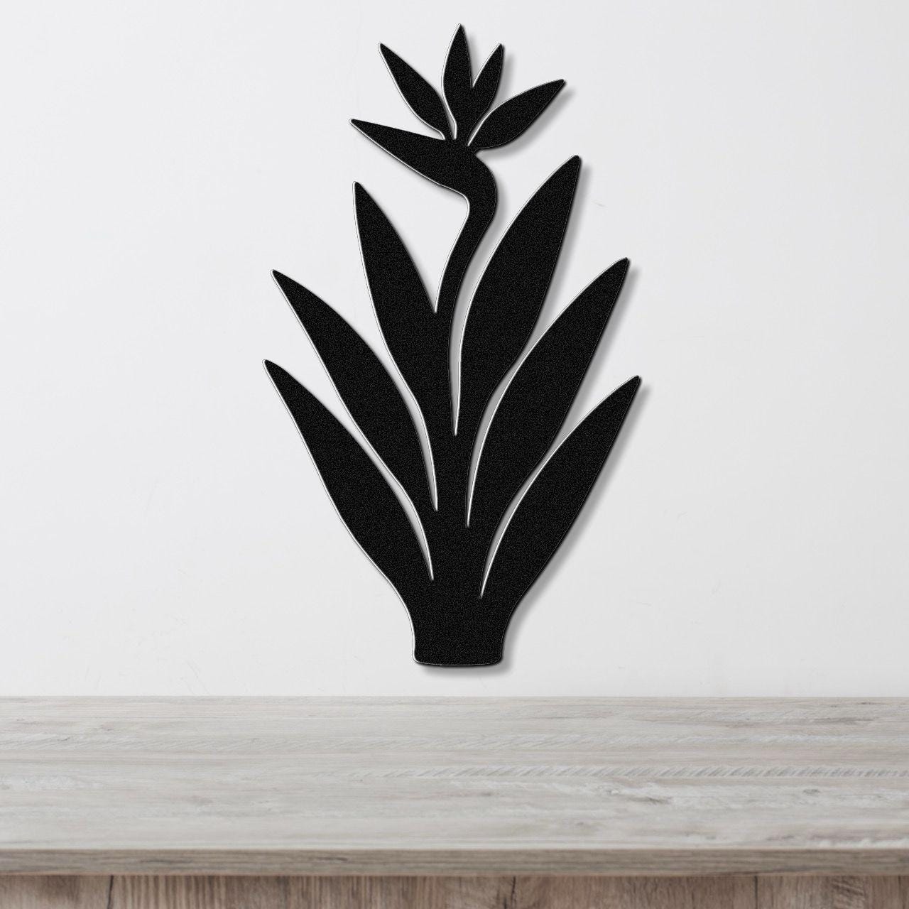 Black metal Bird of Paradise wall art with a silhouette cutout of leaves and flower, mounted on a white wall above a light wood counter.