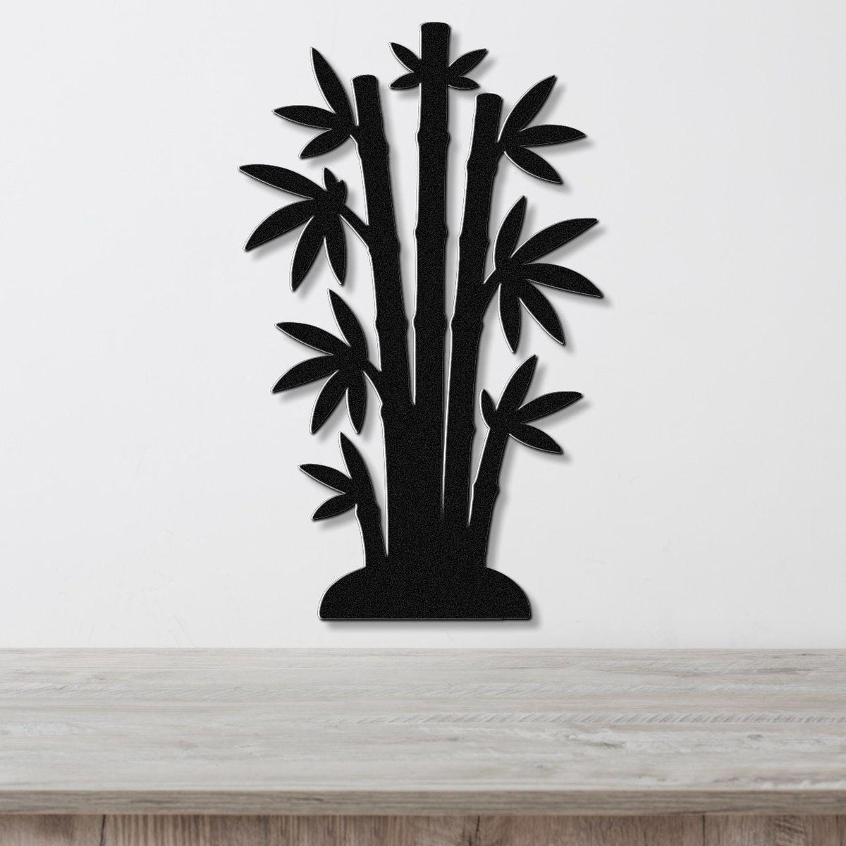 Black metal wall art cutout of a bamboo cluster with multiple stalks and leaves, mounted on a white wall above a light wood surface.