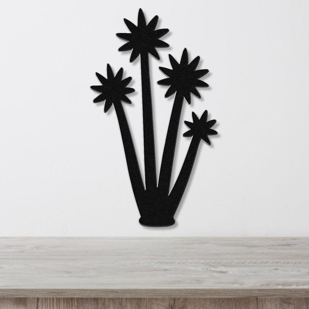 Black metal wall art cutout of a tall yucca plant with star-shaped blooms, mounted on a white wall above a light wood surface.