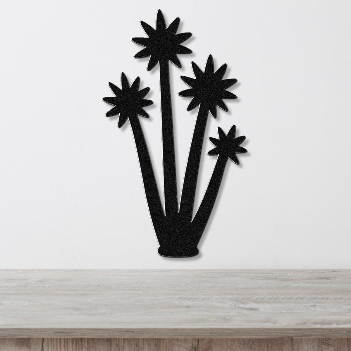 Black metal wall art cutout of a tall yucca plant with star-shaped blooms, mounted on a white wall above a light wood surface.