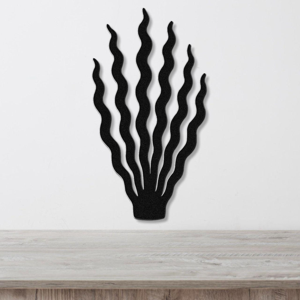 Black metal wall art in a kelp or seaweed silhouette with wavy, flowing strands, mounted on a white wall above a light wood surface.