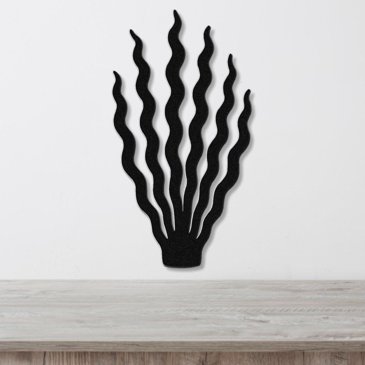 Black metal wall art in a kelp or seaweed silhouette with wavy, flowing strands, mounted on a white wall above a light wood surface.