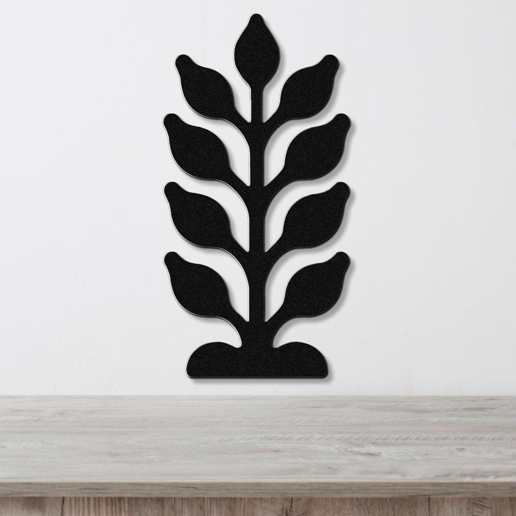 Black metal wall art in a kelp or seaweed silhouette with layered leaf cutouts, mounted on a white wall above a light wood surface.