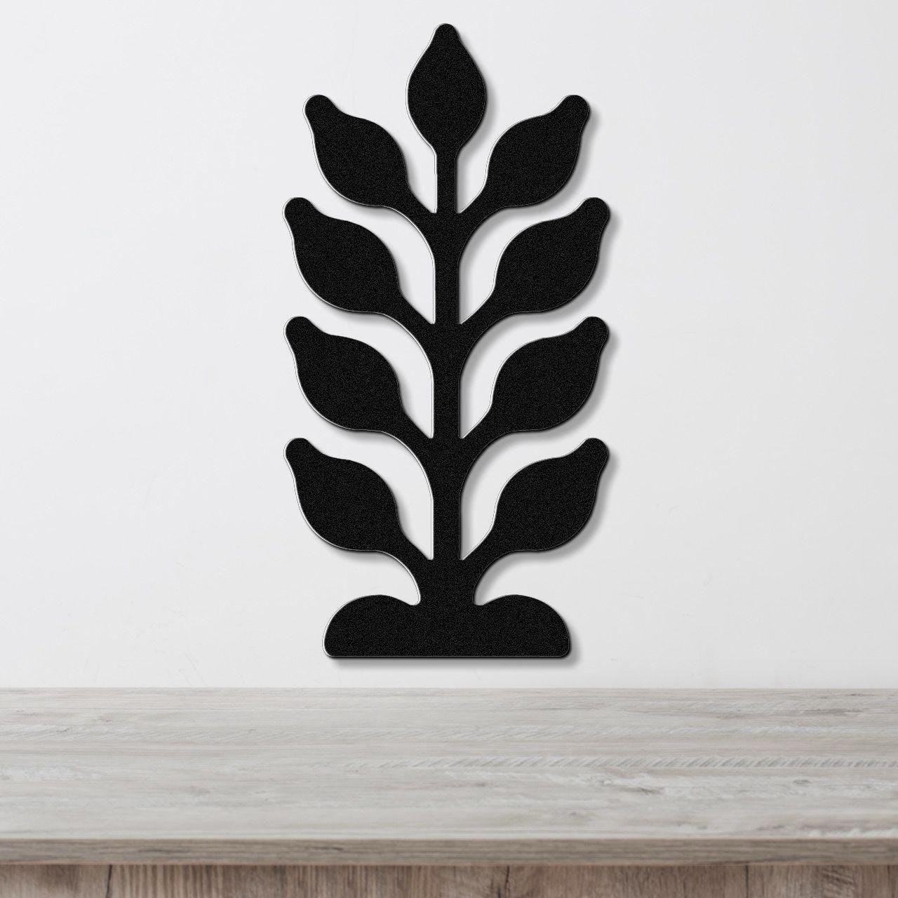 Black metal wall art in a kelp or seaweed silhouette with layered leaf cutouts, mounted on a white wall above a light wood surface.