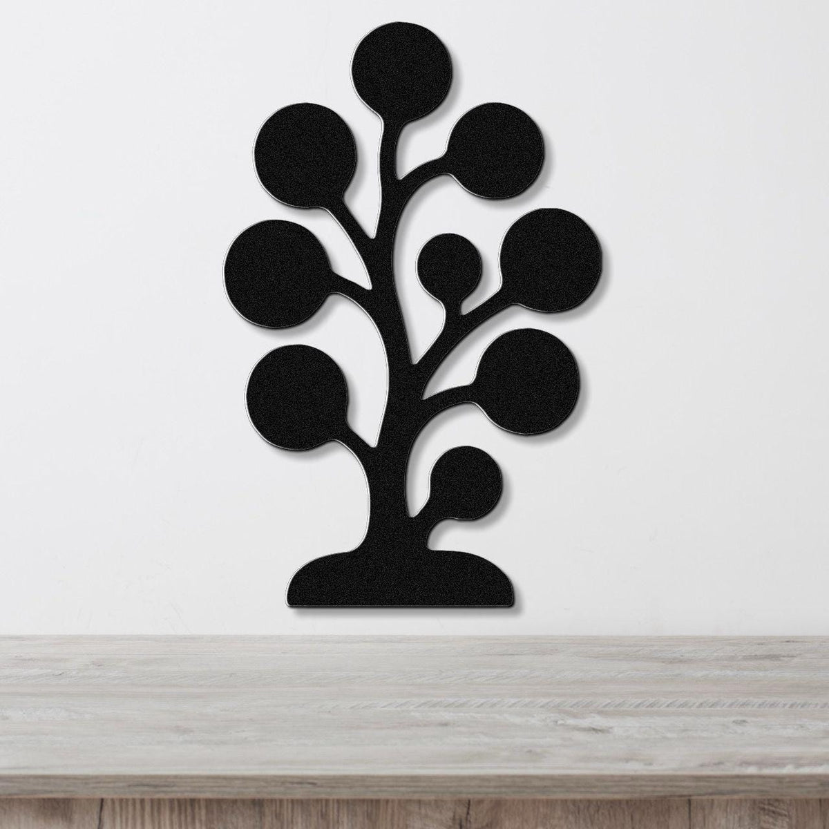 Black metal wall art in a tree silhouette with circular cutouts, mounted on a white wall above a light wood counter.