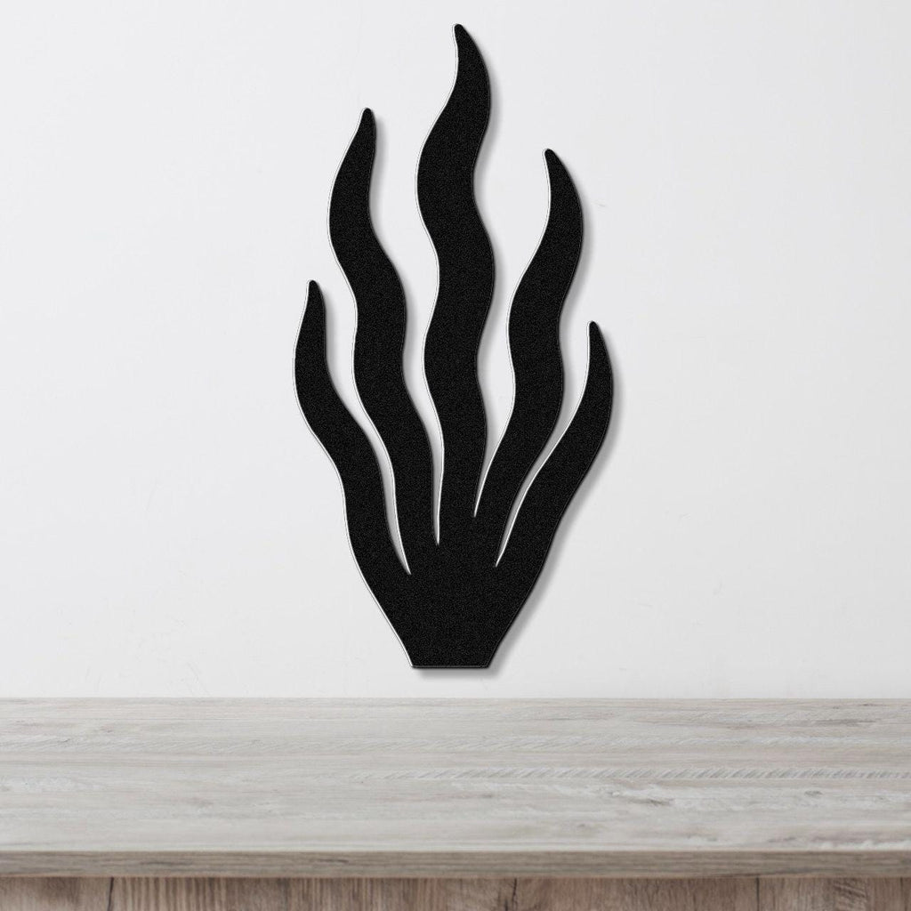 Black metal wall art in a kelp or seaweed silhouette with flowing, wavy fronds, mounted on a white wall above a light wood surface.