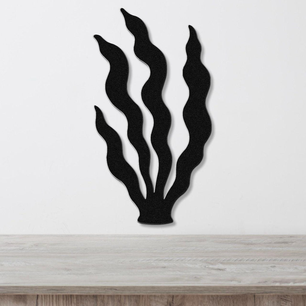 Black metal wall art in a kelp silhouette design with wavy fronds, mounted on a white wall above a light wood surface.